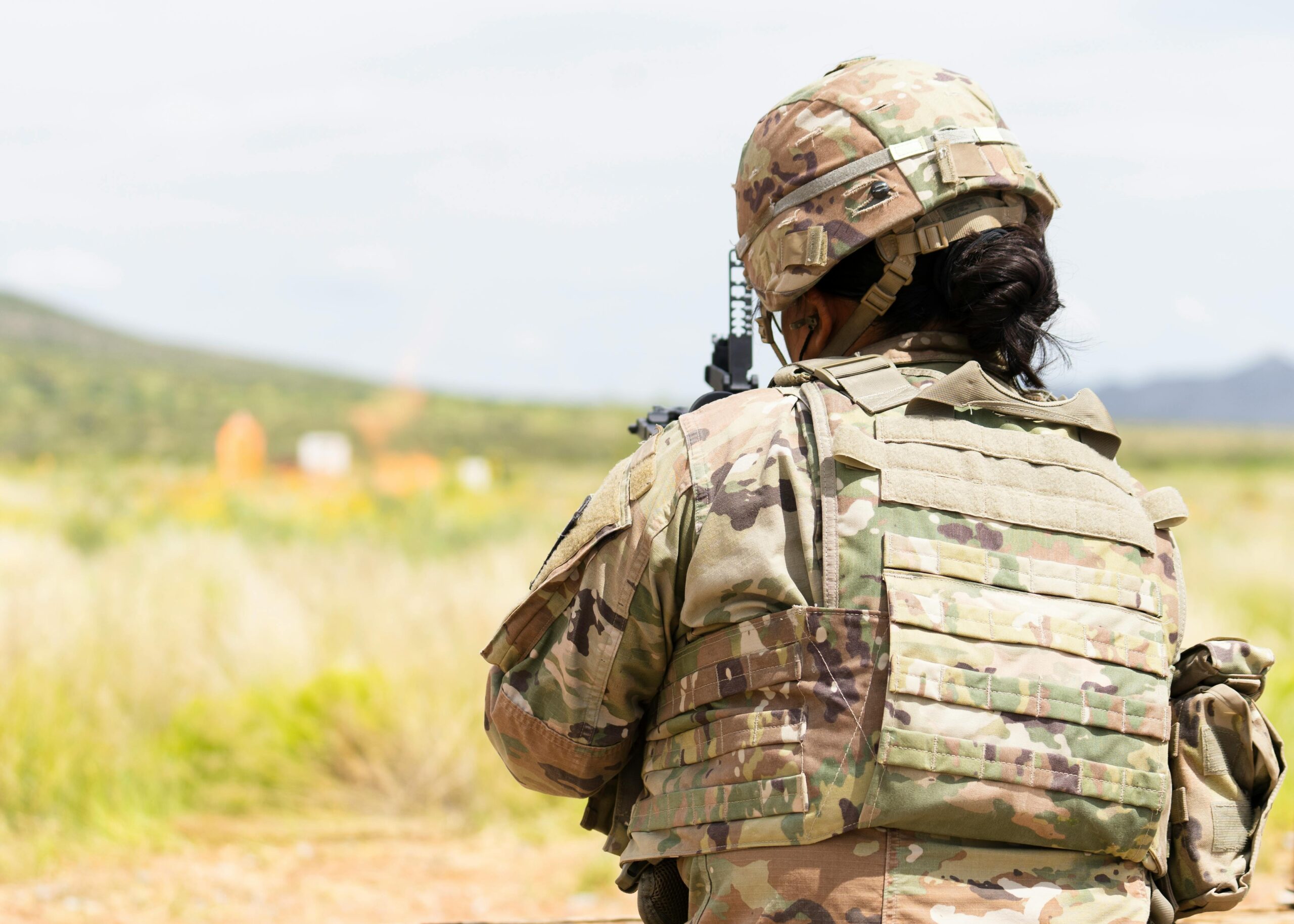 A soldier in a ballistic vest and camouflage uniform training outdoors at Fort Bliss.